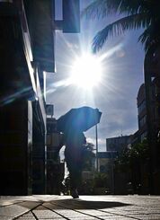 照り付ける朝日のもと日傘をさす女性＝６月２０日午前７時ごろ、那覇市松尾・国際通り