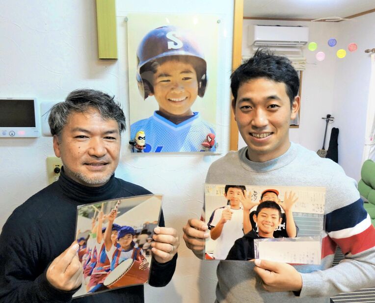 野球少年だった故松田拓哉さんの写真と共に写る父の哲哉さん（左）と、幼なじみの北村勇拓さん＝９日、読谷村内の松田さん宅