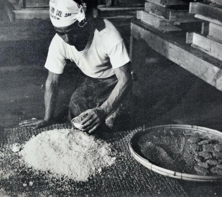 ニクブクの上で蒸された米に黒麹菌を混ぜ合わせる作業工程＝１９５５年ごろ（県酒造組合提供）