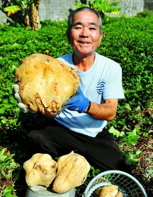 収穫した約７キロの巨大サツマイモを手に笑顔の野里光正さん