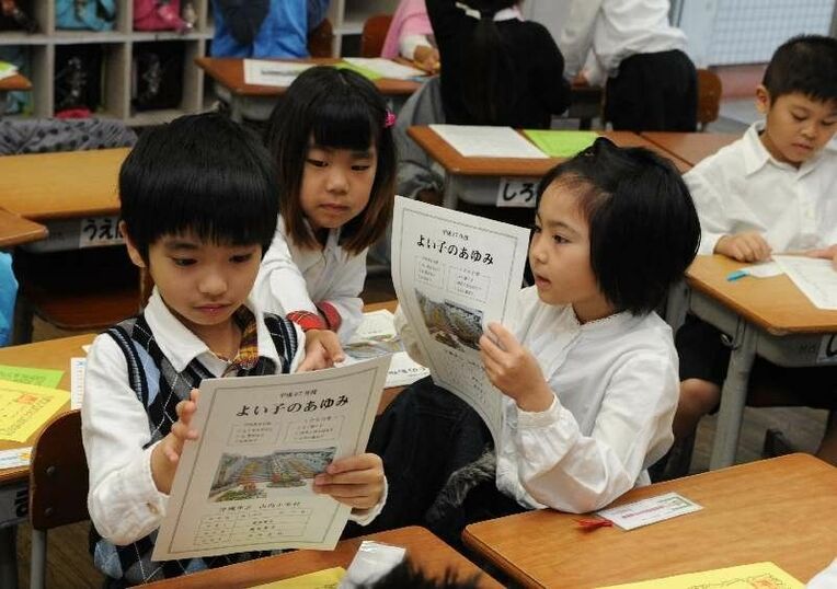 修了式後に手渡されたよい子のあゆみを眺める児童たち＝２４日午前１０時ごろ、沖縄市・山内小学校