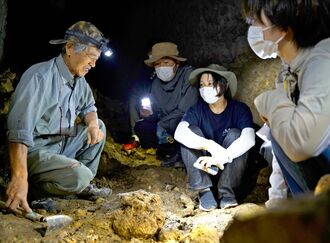 具志堅隆松さん（左）から遺骨収容作業の説明を受ける福島県などの若者世代＝１６日、糸満市の陣地壕