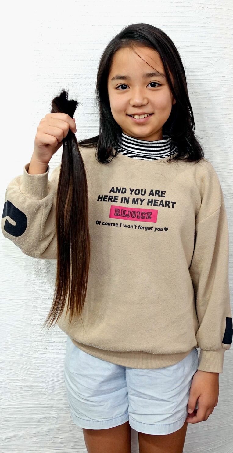 カットされた髪の毛を手に笑顔を見せる新垣琉愛さん＝１６日、宜野湾市の美容室「クラン　ヘアー＆スタジオ」