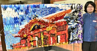折り鶴を貼って作った首里城のモザイクアートと、寄贈に感謝する安里成哉係長＝首里城公園