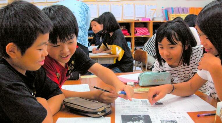 「沖縄全戦没者追悼式」を報じる全国紙の１面を読む児童たち＝３日、沖縄市立比屋根小学校