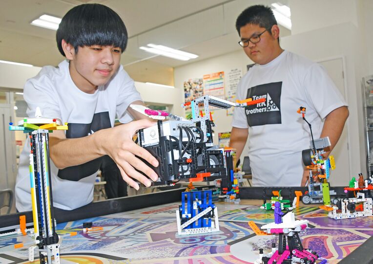 全国大会を控え、ロボットをフィールドに置いて動きを調整する喜瀬青也さん（左）＝１１日午後、南風原町津嘉山のキックス×クレファス・サンエーつかざんシティ校