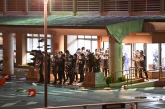 盾を持った警察官が並び、玄関を防御する沖縄署。若者たちによる投石でガラスにひびが入った箇所も確認できる＝２８日午前２時１５分、沖縄市
