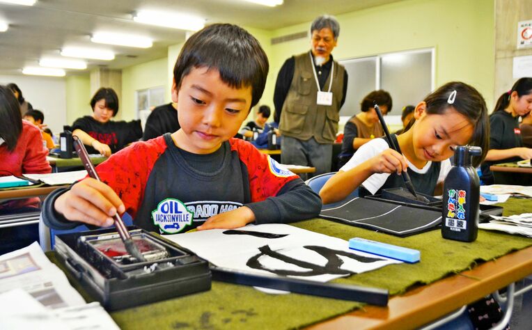 真剣な表情で筆を走らせる子どもたち＝２１日、沖縄市中央公民館