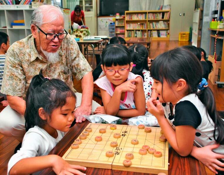 吉川正一さん（左）に教わりながら、象棋（チュンジー）の対戦をする長田児童クラブの子供たち＝１０日、那覇市長田
