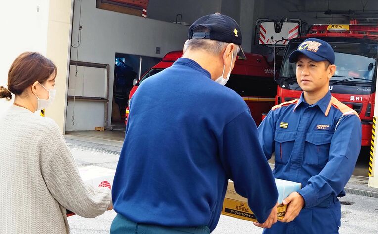 司令補の安慶名隼人さん（右）に飲み物などを手渡すあいあいの利用者ら＝うるま市・具志川消防署