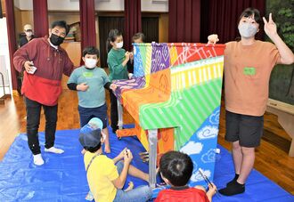 アルベルト城間さん（左）とピアノに色を塗る子どもたち＝南城市・津波古公民館
