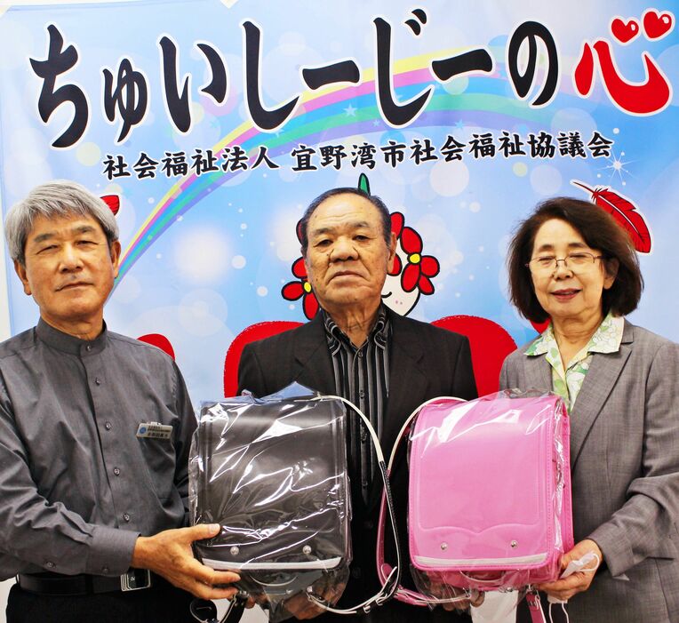多和田眞光会長（左）にランドセルを贈る禰覇忠弘さん（中央）＝宜野湾市
