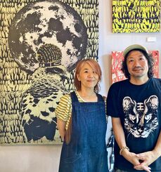 シルクスクリーンパネルをバックに立つ池城安武さん（左）と振角智子さん＝ロンドン・モコメイドカフェ
