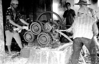 圧搾機を使い、黒糖の原料となるサトウキビの汁を搾り出す美里村古謝の農民たち。古謝は１９３３年、沖縄県から「糖業経営改善指導部落」と指定を受け、サトウキビの品質向上や収穫量増加を目指した。圧搾機は村の農家で構成する「共同製糖組合」が３０年代に購入。利用は１日１世帯に限られており、予約表に基づいて農民たちはサトウキビの収穫日程を調整していたという（写真：朝日新聞社）