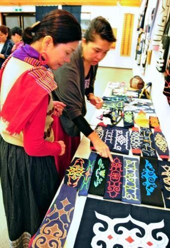 アイヌ伝統工芸作品展が始まり、多くの人が黒や濃紺の生地に曲線の描かれた衣服などを観賞している＝１５日、南風原文化センター