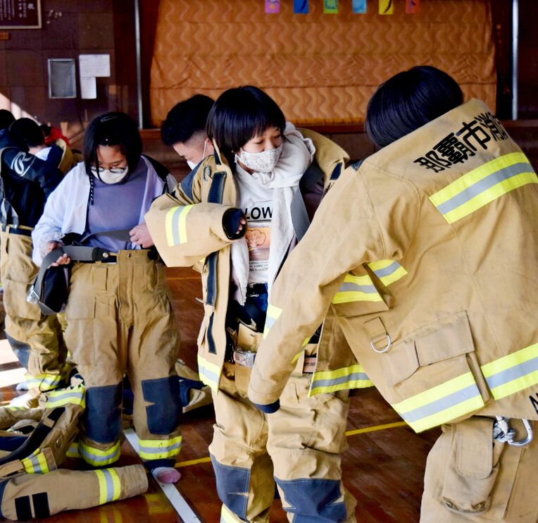 防火服の着用体験と救助訓練をする児童＝１月１８日、西原町・坂田小学校