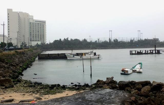 沈んだ船などが放置された「仮設避難港」。奥にはラグナガーデンホテル（左）や海浜公園があり、本島西海岸のリゾートはここで分断されている形だ＝宜野湾市真志喜