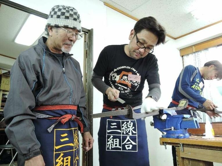 渡慶次理事長（左）から三線作りの指導を受けるひーぷーさん＝２０日、同組合店舗