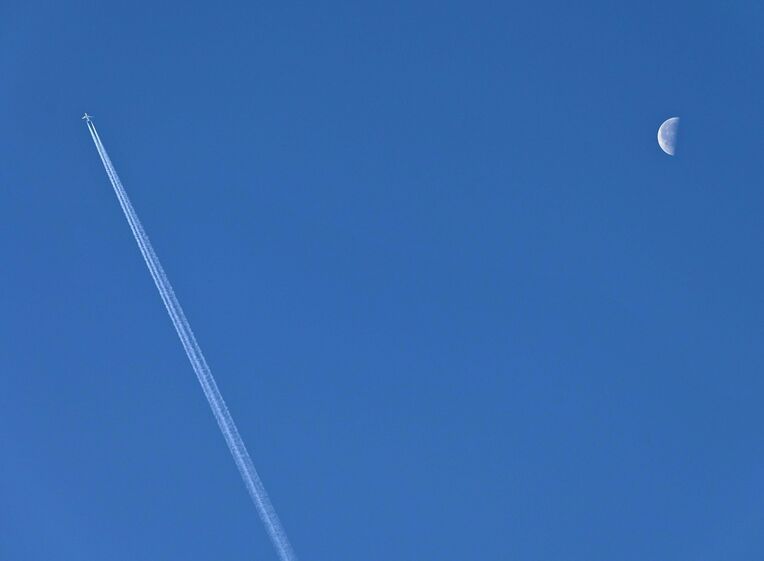 青空に浮かんだ月に向かって伸びる飛行機雲。うまく重なるかなとカメラを構えていましたが、結果はご覧の通りです＝３日、西原町（伊禮健撮影）