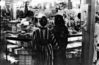 那覇市内にあった雑貨店の様子。庶民が日常的に生活物資を買い求めていた市場とは雰囲気が異なる。市内にいくつかあった百貨店内だろうか。店内にはキューピー人形がディスプレーされているほか、ボンタンアメの広告が確認できるなど、店の品ぞろえの豊富さが分かる。１９３５年当時から、沖縄にも商品経済の波が訪れていたことが見て取れる（写真：朝日新聞社）