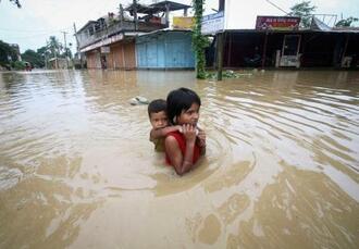 　大雨で浸水した道を、弟を背負って歩く少女＝６月、インド北東部アガルタラ郊外（ロイター＝共同）