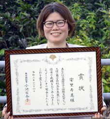 第２５回総合写真展の東京都知事賞の賞状を手にする安里寿美さん＝２２日、中城村